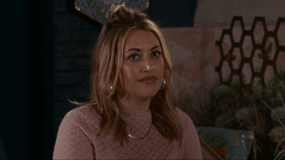 Screenshot of a woman with blonde hair wearing a pink sweater.