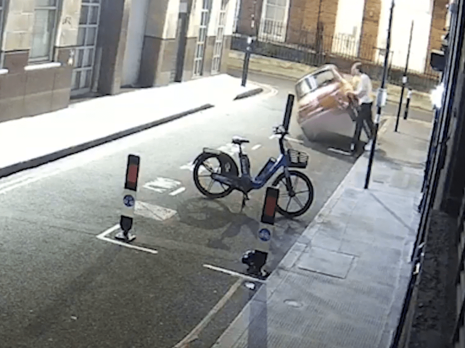Screenshot of a person pushing a car down a street, with a bicycle parked nearby.