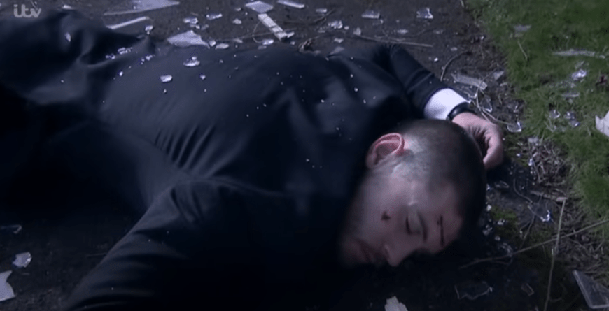 Man lying unconscious on the ground surrounded by broken glass.