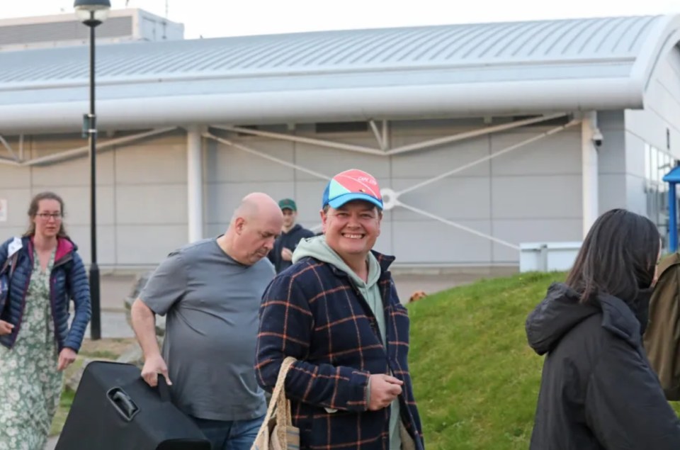 A man smiling while carrying a bag, with other people in the background.