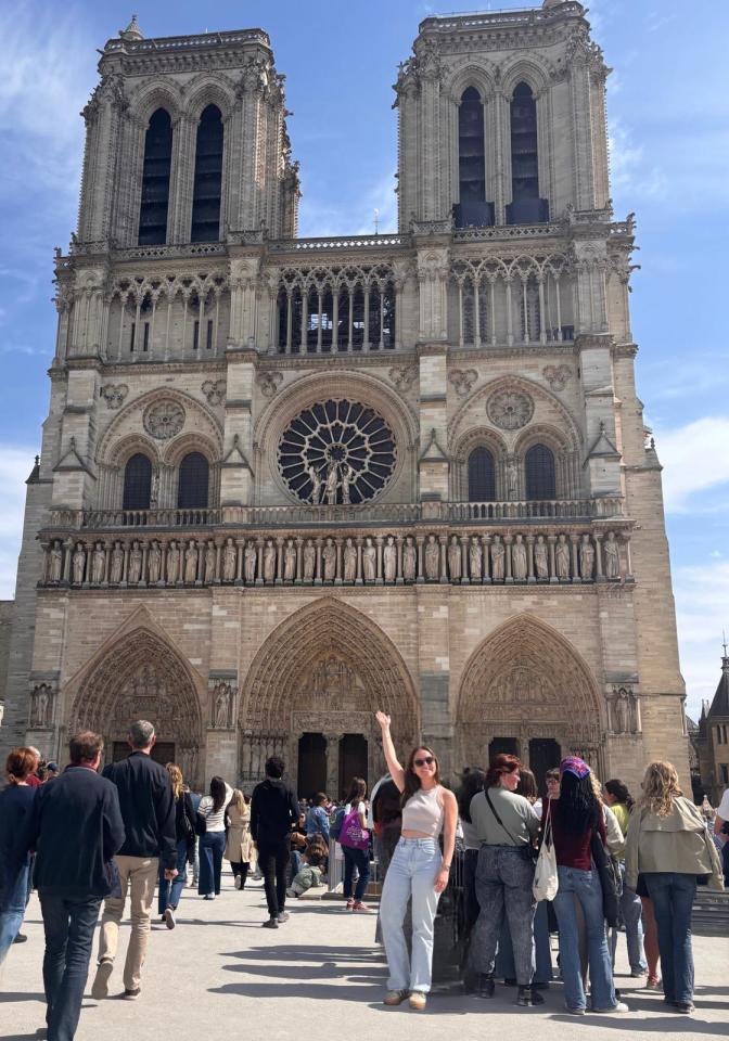 Person waving in front of Notre Dame Cathedral in Paris.