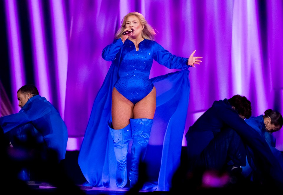 Singer in blue bodysuit and boots performing on stage.