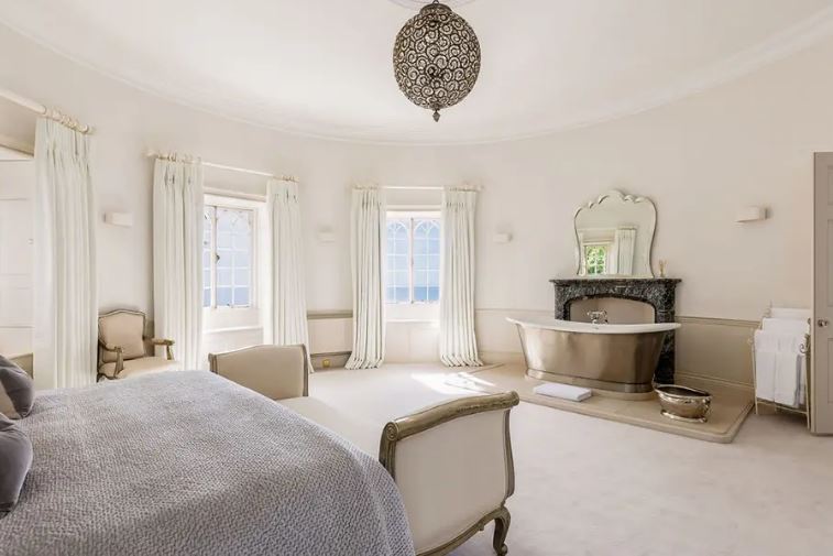 Bedroom with large windows, a freestanding bathtub, and a chaise lounge.