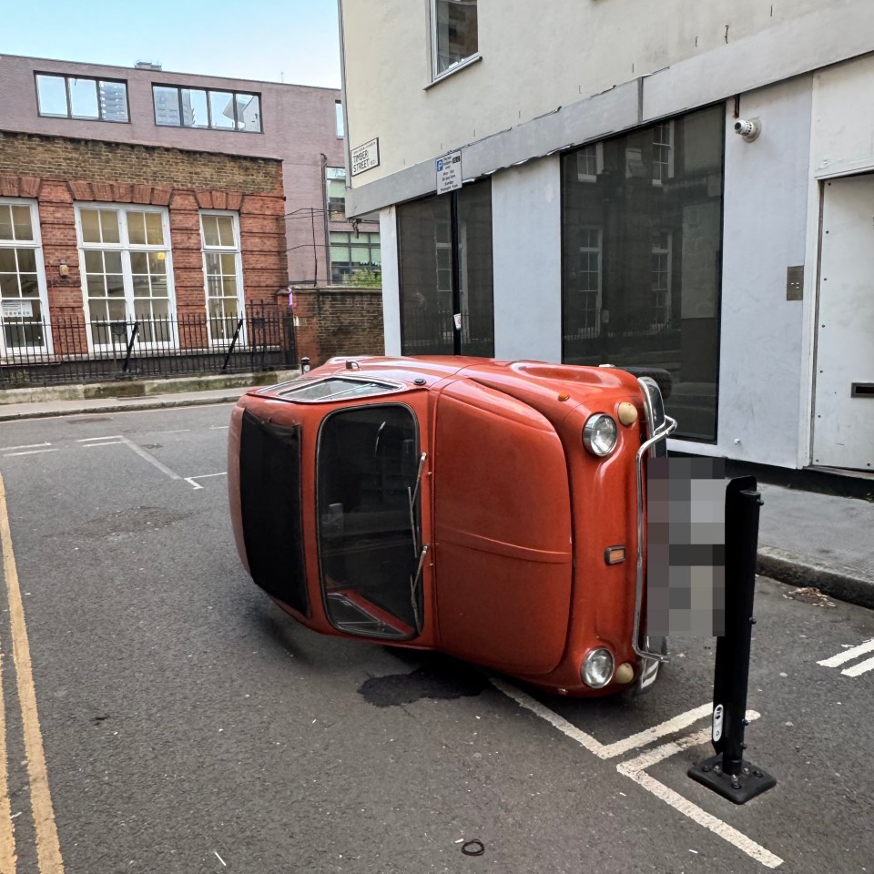 An orange classic car on its side in a parking space.