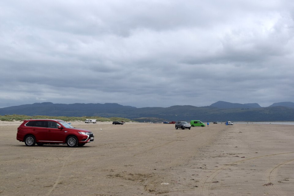 Cars parked on a beach with mountains in the background.