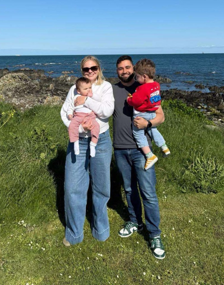 Family photo of parents holding their baby and toddler near the ocean.