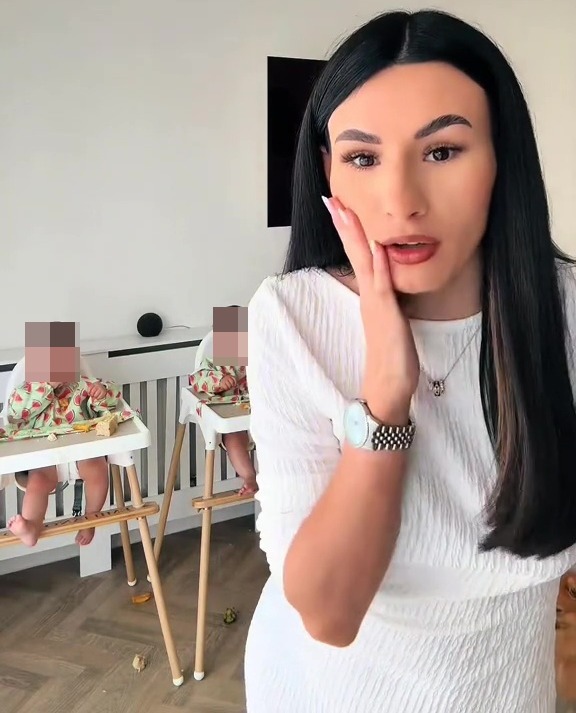 Woman in white dress reacting to her twin babies in high chairs.