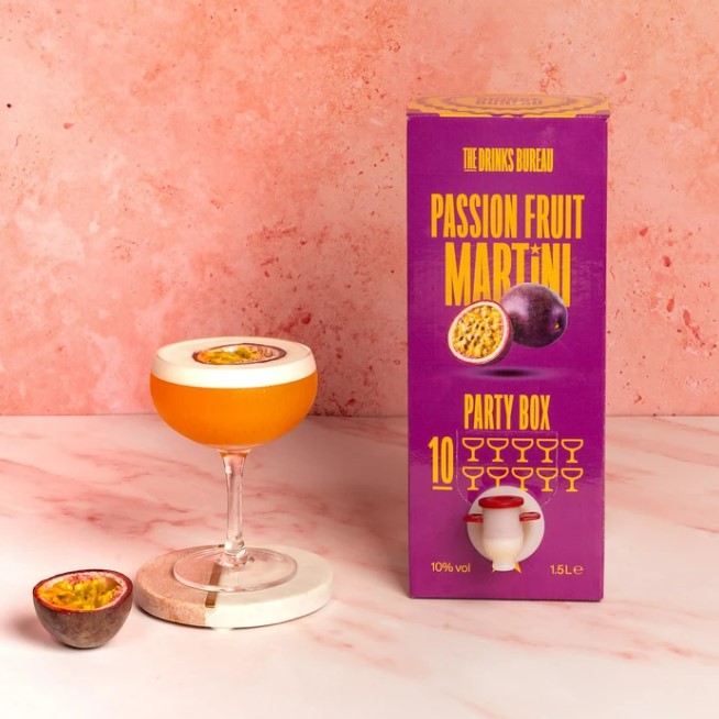 Passion fruit martini cocktail in a coupe glass next to a party box of the same cocktail.