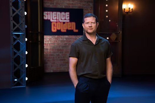 A man standing in front of a "Silence is Golden" sign.