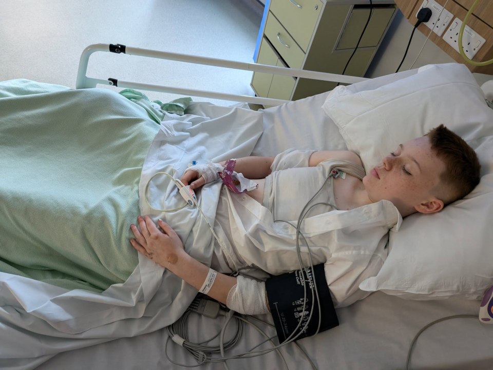 A young boy lying in a hospital bed with medical equipment attached.