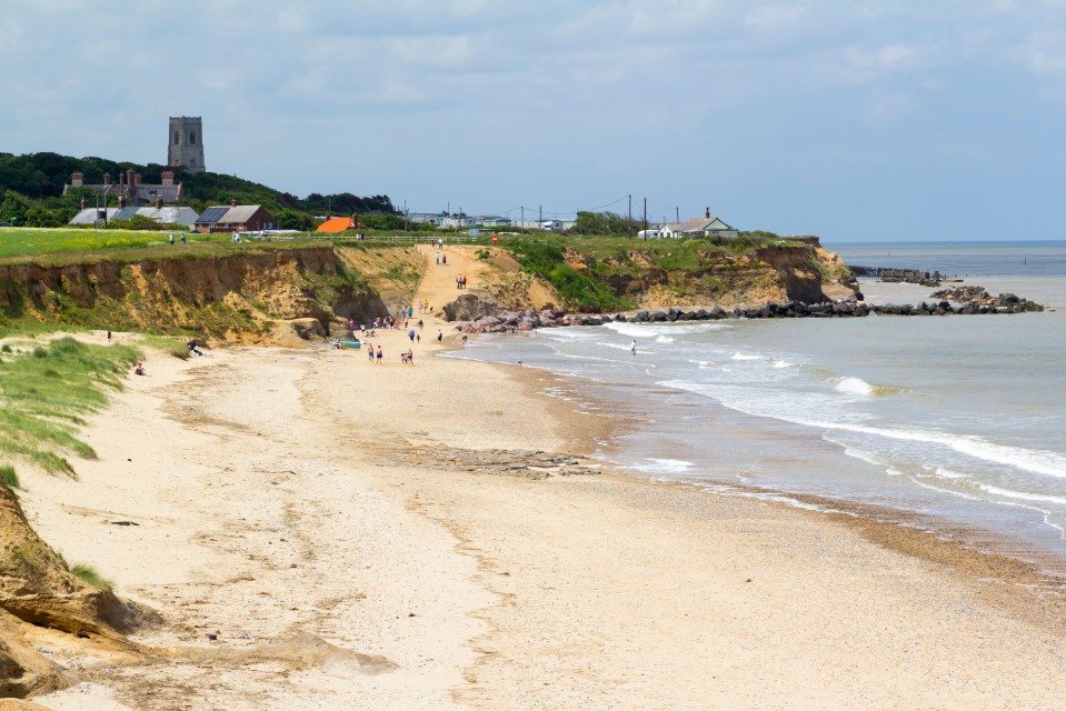 Happisburgh Beach in North Norfolk, England, with people on the sandy beach and a church visible in the distance.