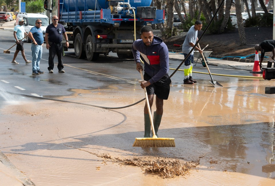 Worker clearing mud from a flooded street.