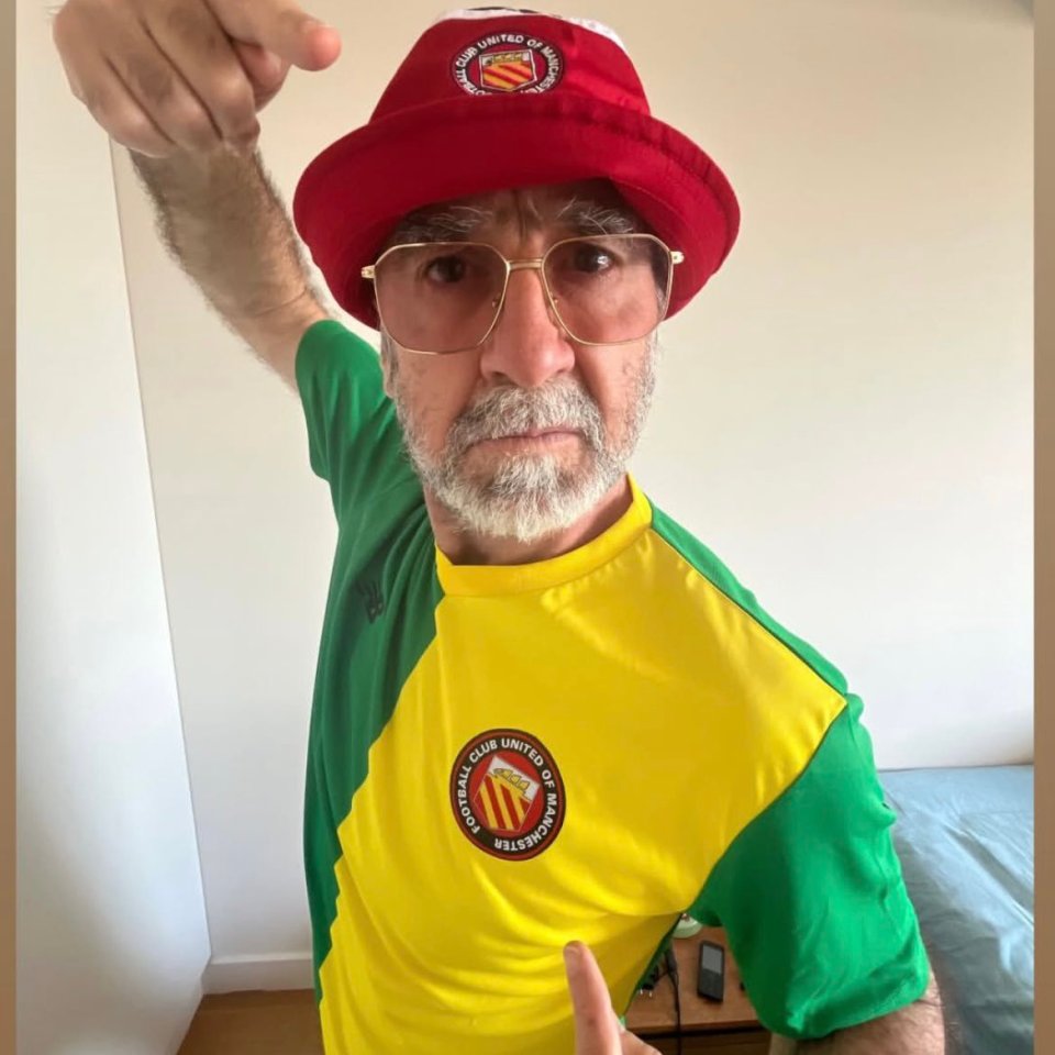 Eric Cantona wearing a Manchester United hat and jersey.