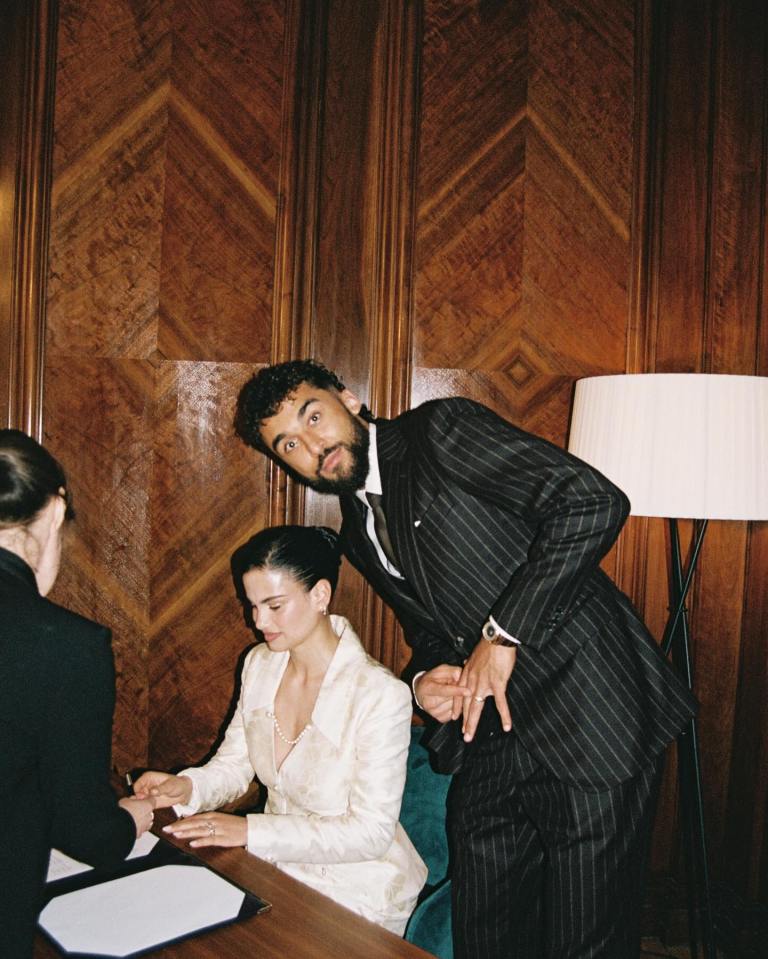 A bride signing documents while a man in a pinstripe suit looks on.