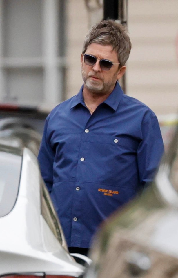 Noel Gallagher wearing sunglasses and a blue shirt.