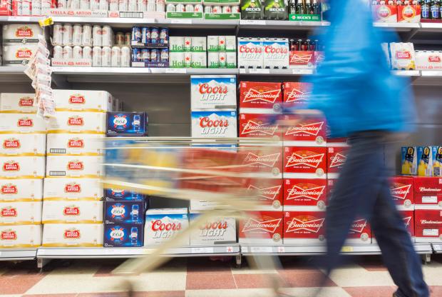 Man pushing a shopping cart full of beer in a supermarket.