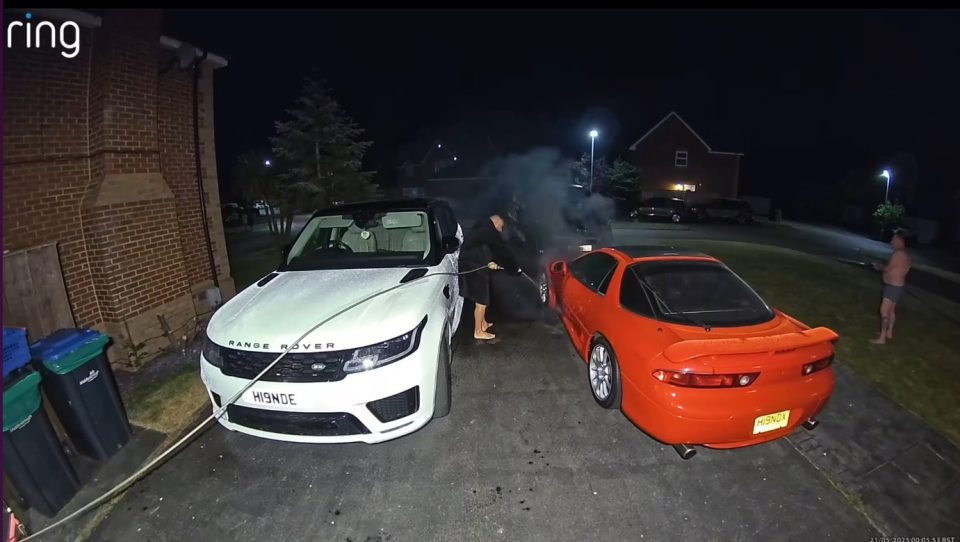 A man hoses down two cars at night after a fire.