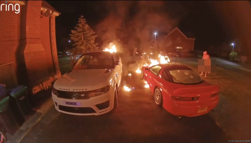 Security camera footage of two cars on fire in a driveway.
