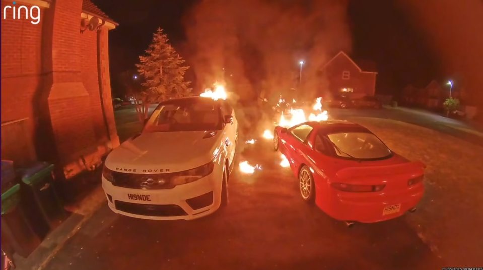 Two cars engulfed in flames in a driveway at night.