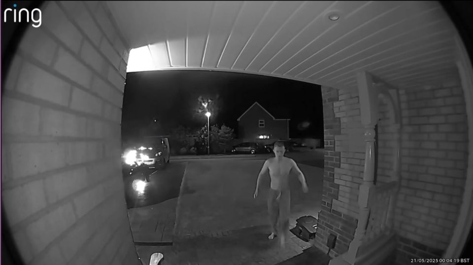 Nighttime security camera footage of a shirtless man walking near a house.