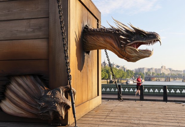 Animatronic dragon head emerging from a wooden structure in front of a clock tower.