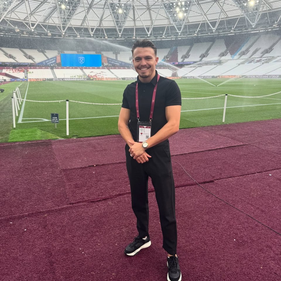 Man in black shirt and pants standing on a soccer field in a stadium.