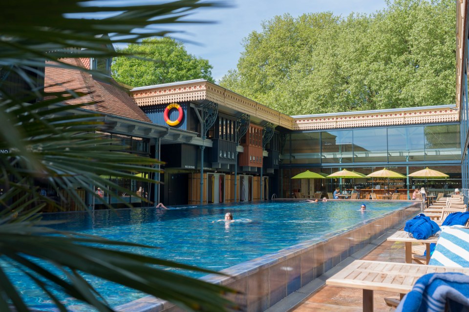 Outdoor swimming pool with people swimming and a cafe in the background.
