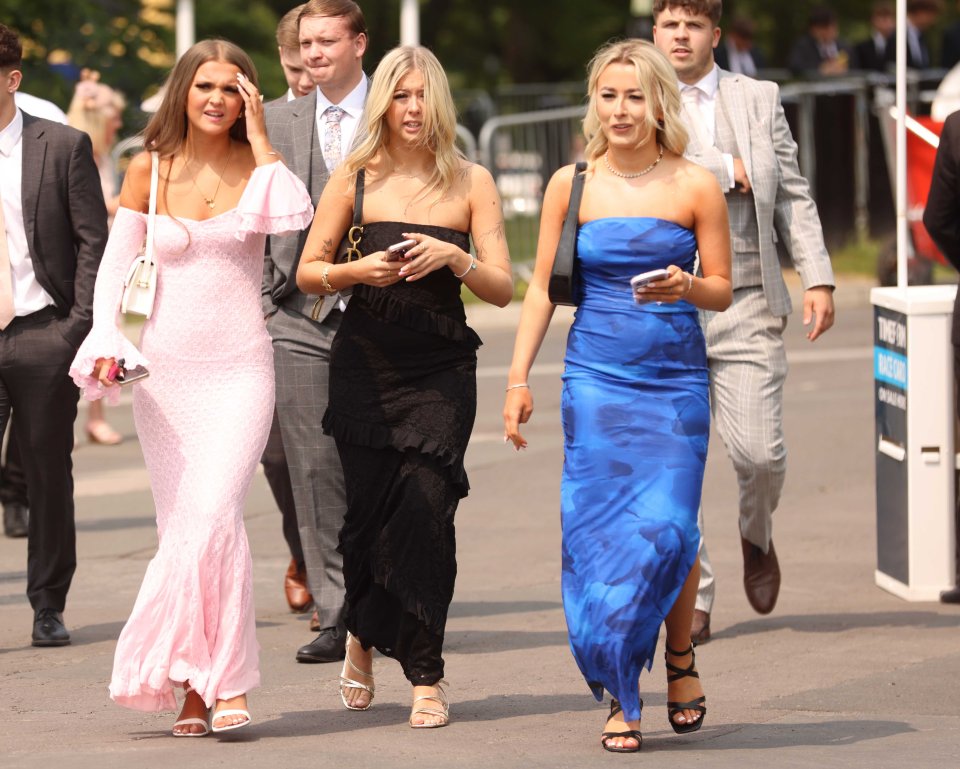 Three women in dresses and two men in suits walking at a racecourse.