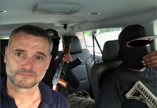A man in a vehicle with two armed men.