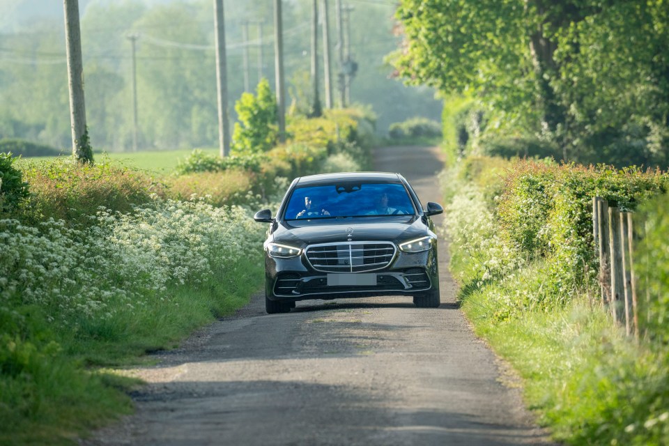 A black Mercedes sedan driving down a country lane.