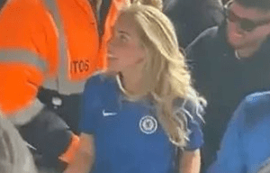 Woman in Chelsea jersey surrounded by people.