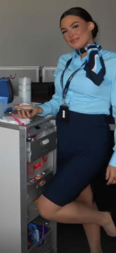 Flight attendant in uniform next to a beverage cart.