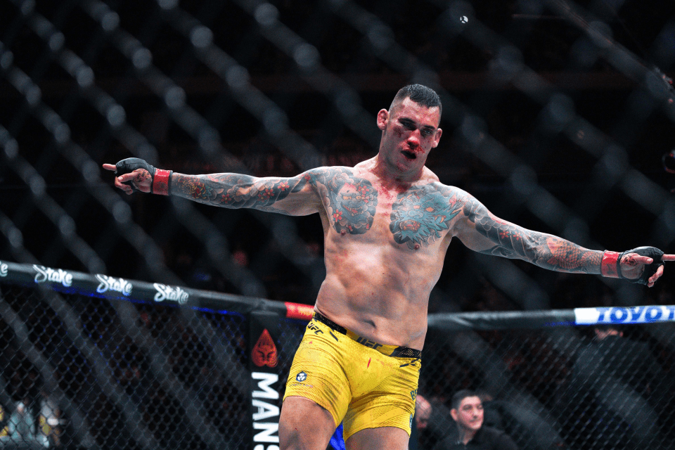 A bloodied MMA fighter with tattoos celebrates in the octagon.