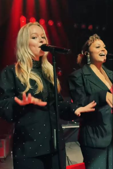 Two women singing into microphones on stage.