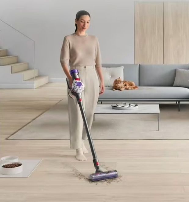 Woman vacuuming floor with cordless vacuum cleaner.