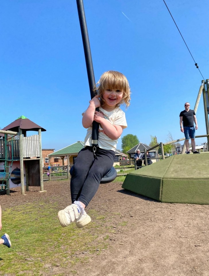 Smiling toddler on playground zipline.