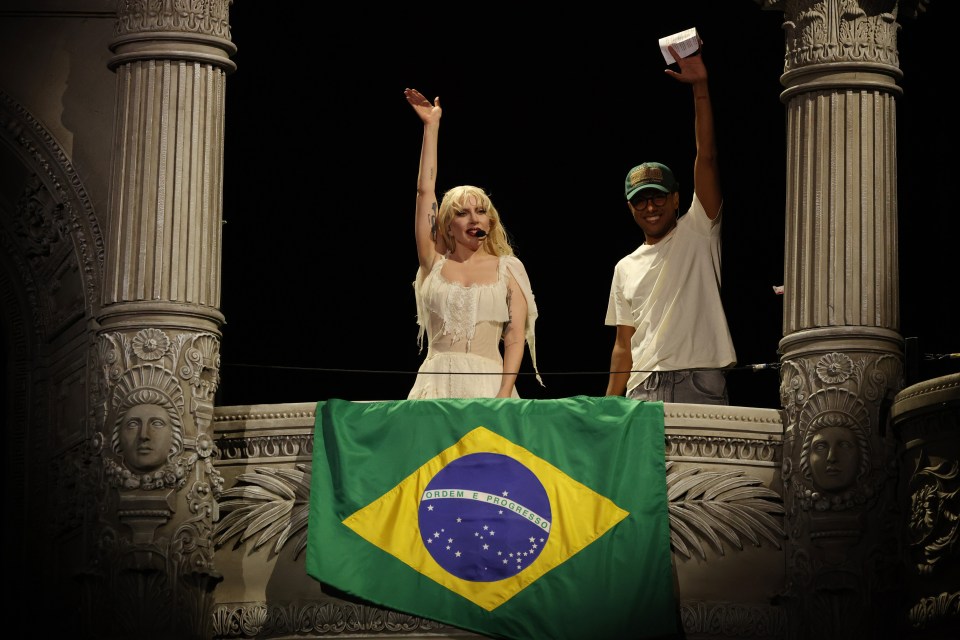 Lady Gaga and a man holding a Brazilian flag on a balcony.