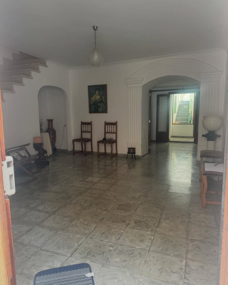 Interior view of a tiled room with stairs, arched doorway, and furniture.