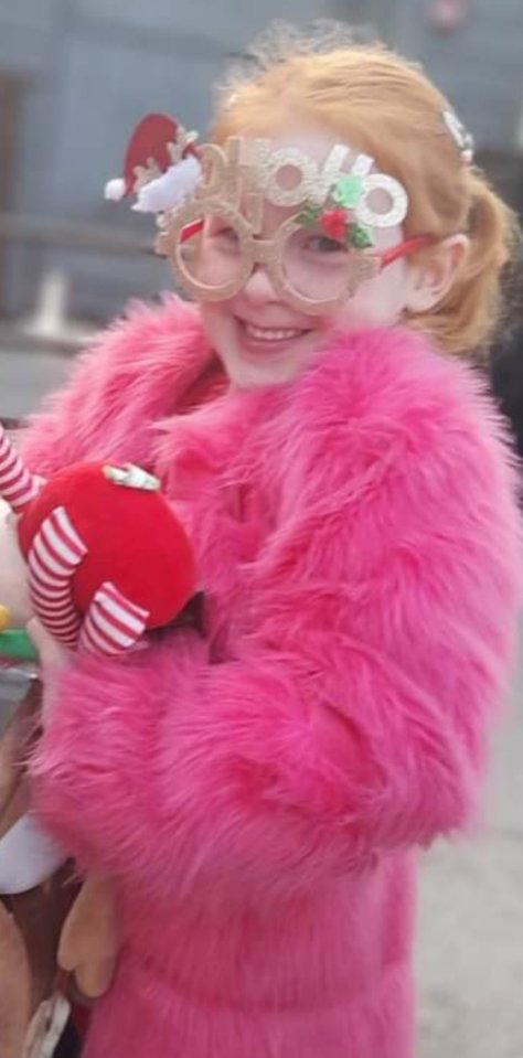 Girl in pink fluffy coat wearing holiday glasses.