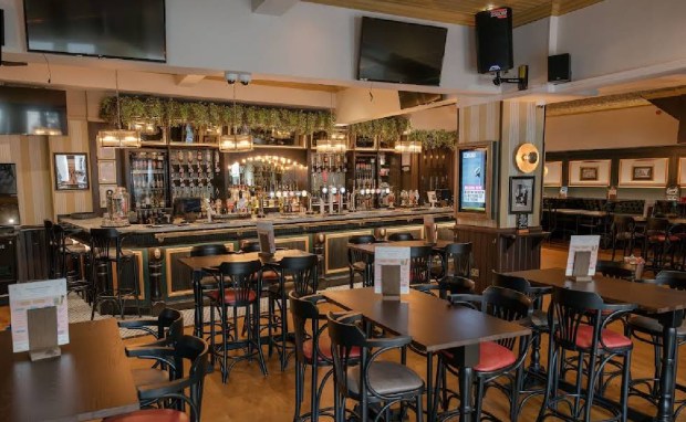 Interior view of a pub with a long bar, multiple tables and chairs, and televisions.