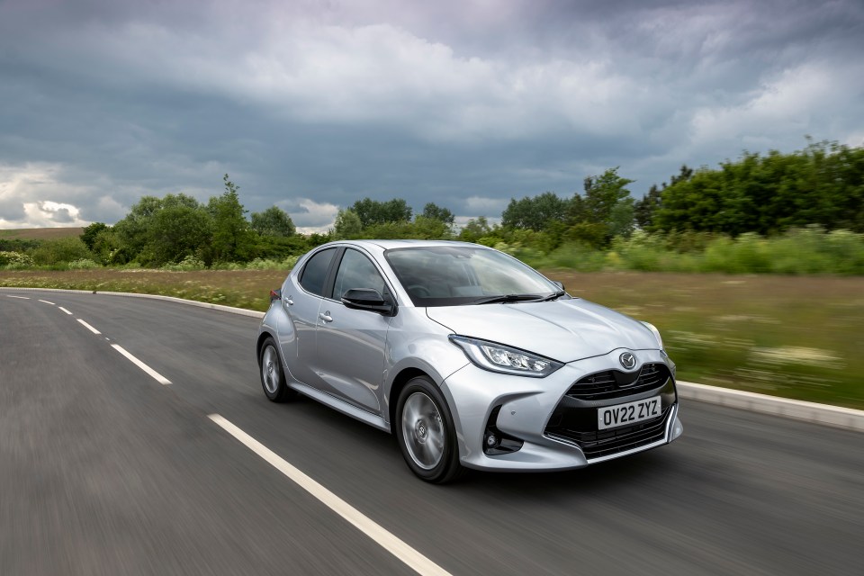Silver Mazda 2 hybrid driving on a road.