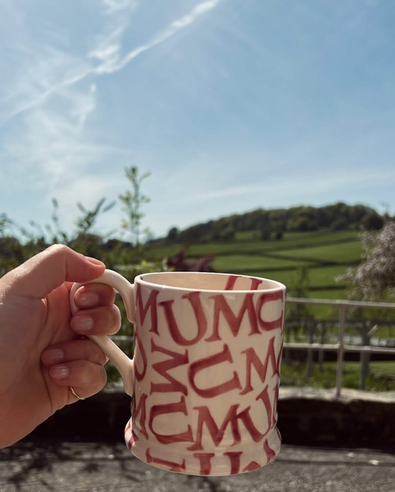Hand holding a mug with red letters against a blurry outdoor background.