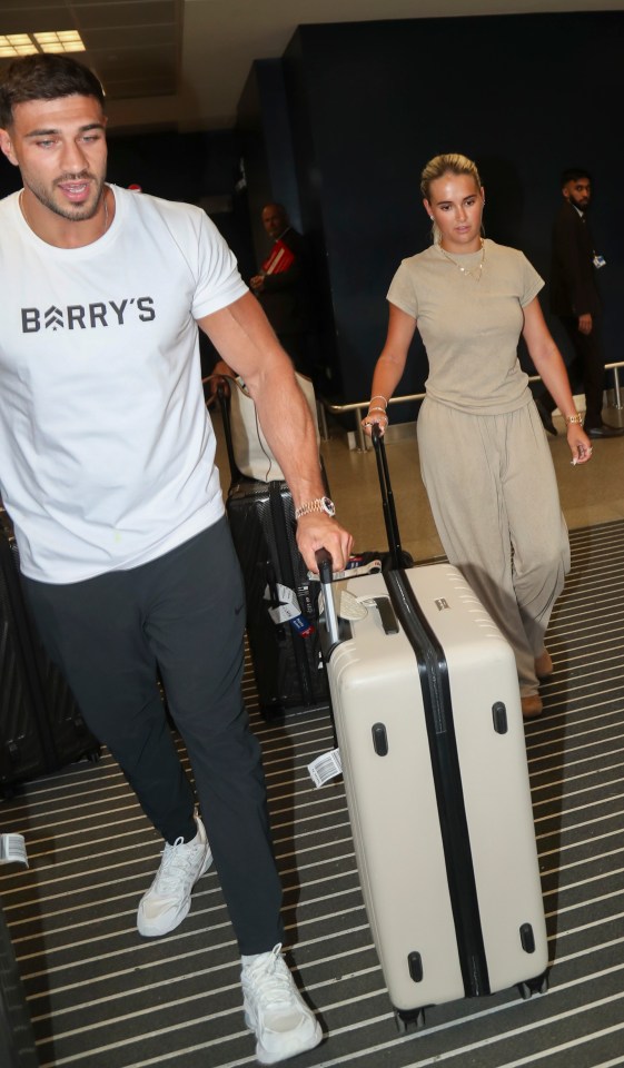 Molly Mae and Tommy Fury arriving at an airport with luggage.