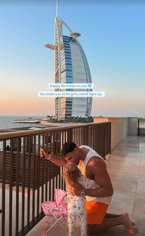 A man kneeling and kissing a toddler on a balcony overlooking the Burj Al Arab.  A birthday message is overlaid on the image.