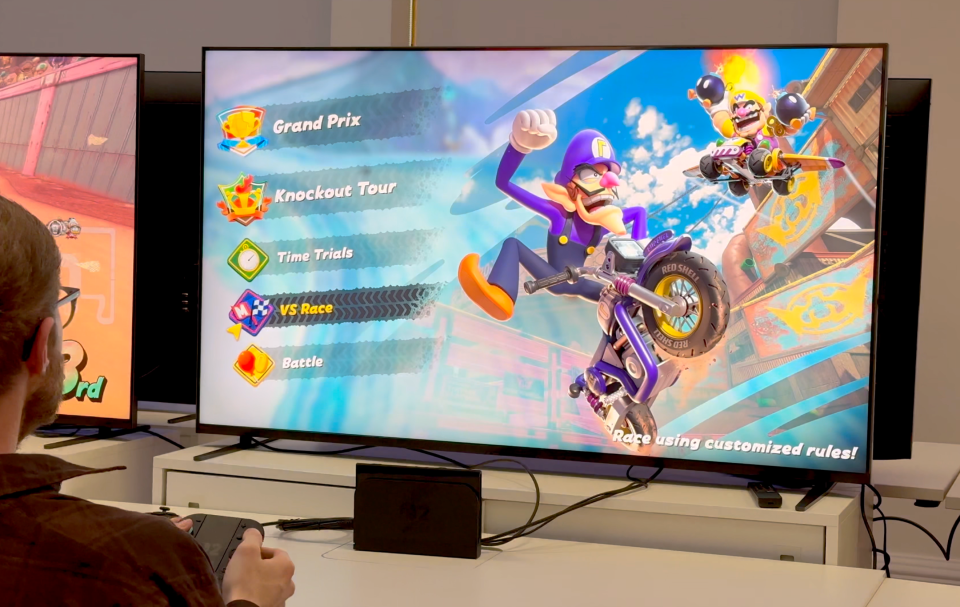 Person playing Mario Kart game on a large screen.