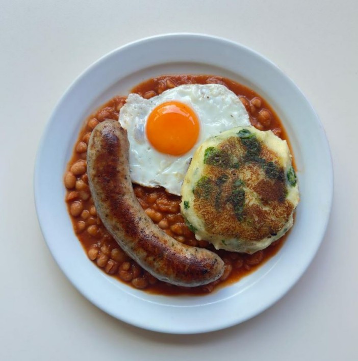 Breakfast plate with sausage, fried egg, baked beans, and potato cake.