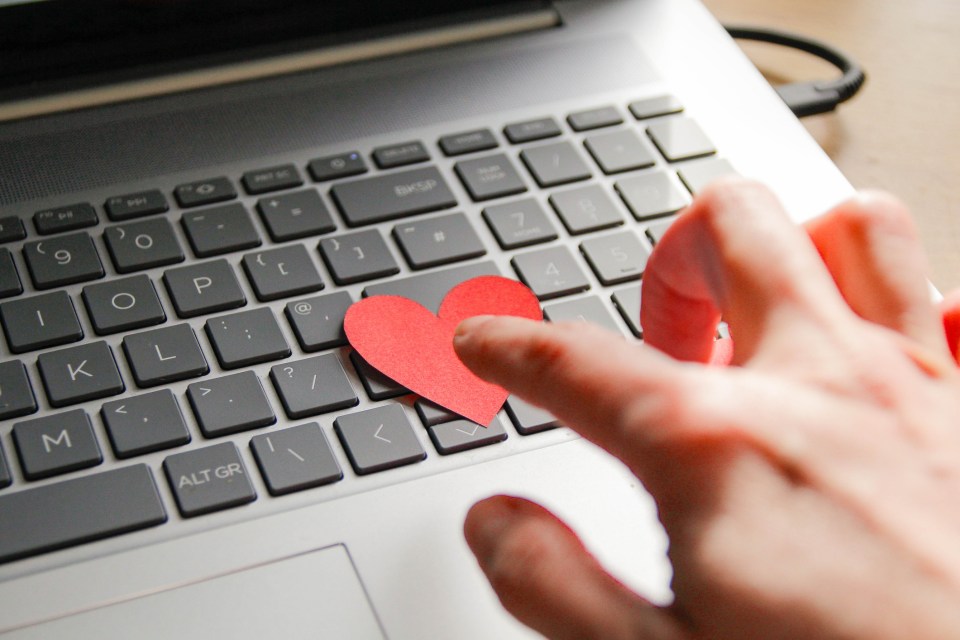 A hand placing a paper heart on a laptop keyboard.