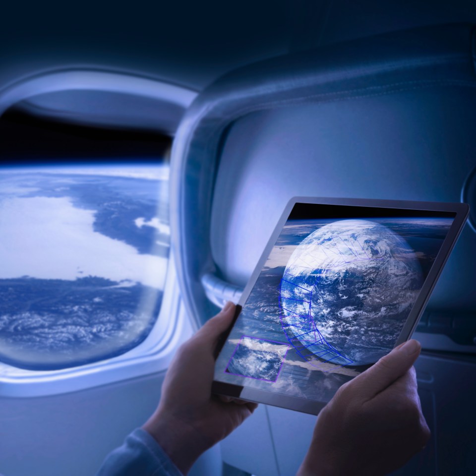 Person on a spaceship looking at a tablet showing Earth.
