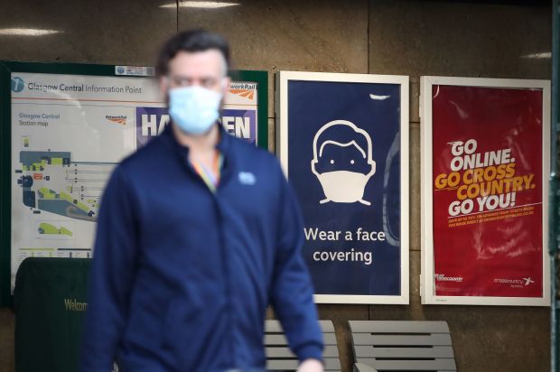 Person wearing a face mask walks past signs in a train station.