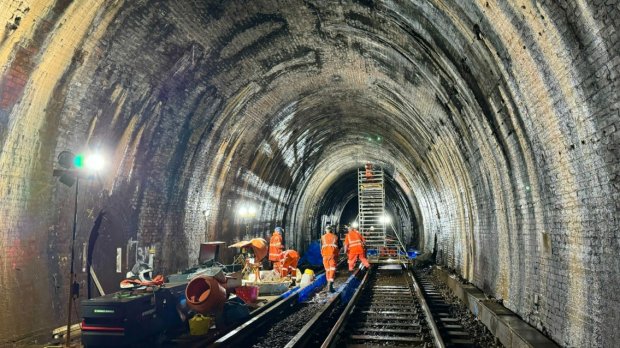 Workers repairing a brick railway tunnel.